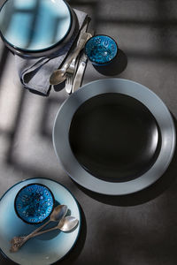 Tableware, different plates in grey blue colors on dark table with geometrical shapes shadows