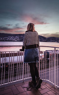 Rear view of woman standing at beach against sky during sunset