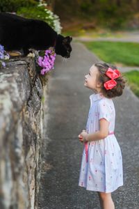 Little girl and black cat looking at each other.