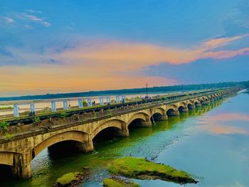 Arch bridge over river against sky during sunset