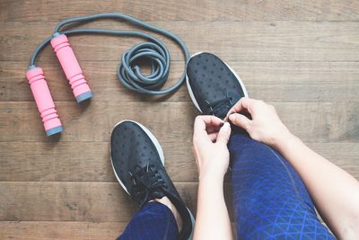 Low section of woman tying shoelace by skipping rope on hardwood floor