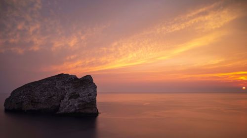Scenic view of rock in sea against sky during sunset