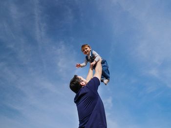 Low angle view of father playing with son against sky