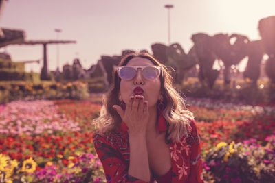 Young woman blowing kiss while standing in ornamental garden 