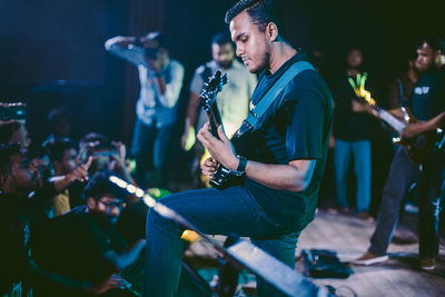 Side view of man playing a guitar on stage during a live rock concert 