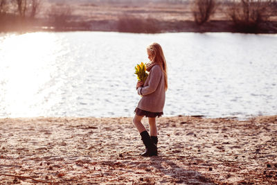 Side view of cute girl holding flowers by lake