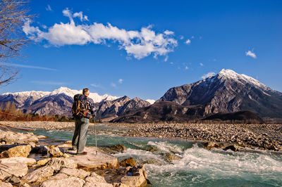 Rear view of man standing on rock by river against sky