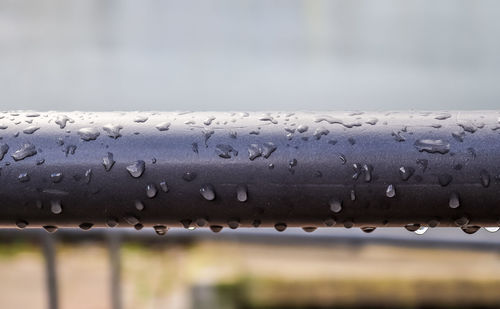 Close-up of raindrops on railing against sky during rainy season