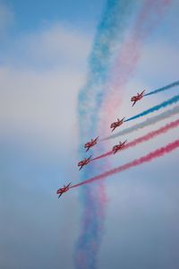 Red arrows in formation with red white and blue vapor trail in sky perform at airshow