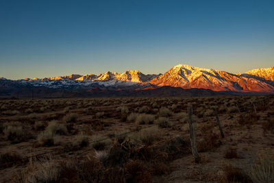 Scenic view of arid landscape and dawn light illuminating snowy mountains against clear sky