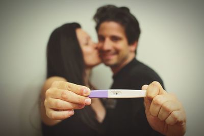 Happy couple holding pregnancy test kit while standing against wall