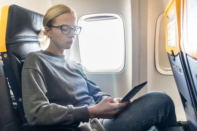 Mid adult woman using smart phone while sitting at airplane