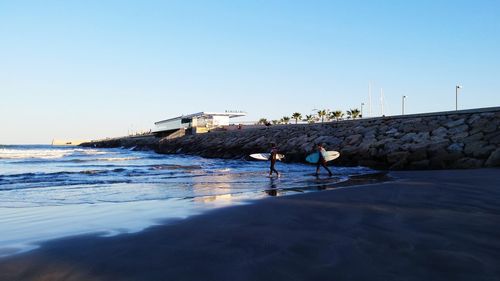 Side view of man and woman with surfboards walking at beach