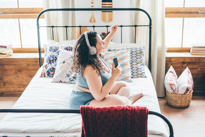 Full length of young woman sitting on bed