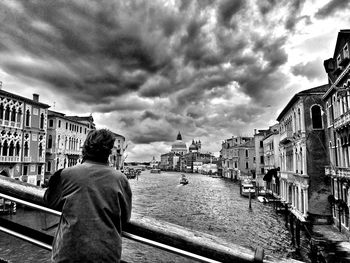 Canal in front of city against cloudy sky