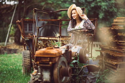 Young woman sitting on abandoned vehicle at field