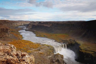 Scenic view of waterfall against cloudy sky