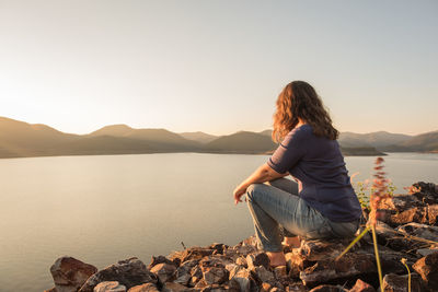 Woman sitting by lake against clear sky