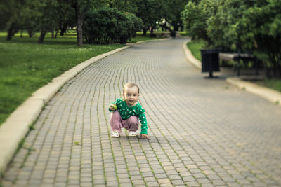 Full length of baby girl looking away while crouching on footpath