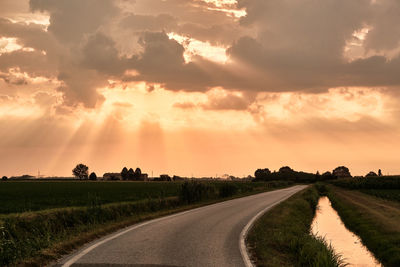 Road amidst field against sky during sunset