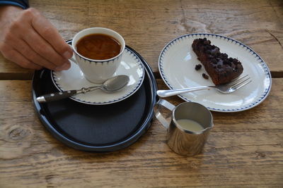 Cropped image of man holding coffee cup by pastry kept in plate