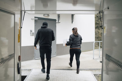 Rear view of male and female workers carrying boxes while walking out of delivery van