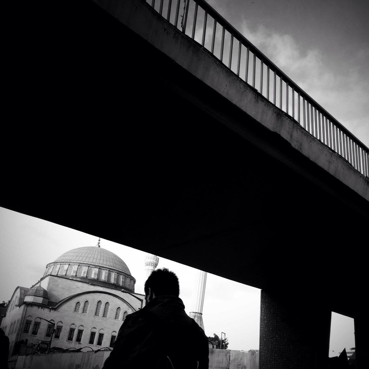 architecture, built structure, lifestyles, men, standing, leisure activity, building exterior, low angle view, railing, rear view, person, bridge - man made structure, walking, sky, casual clothing, city, low section