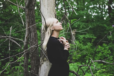 Young woman standing by tree trunk in forest