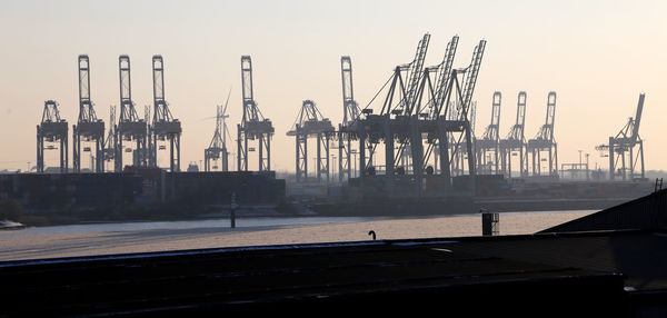 Cranes at harbor against sky