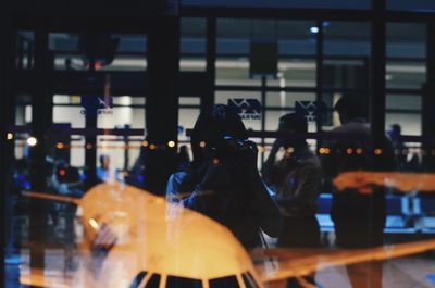 Woman photographing airplane with reflection on window glass at airport