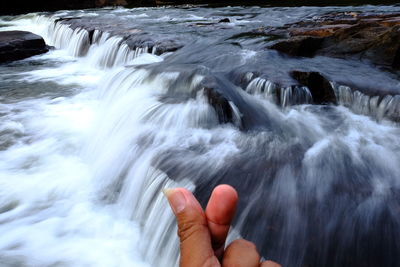 Cropped image of hand against waterfall