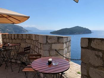 Empty chairs and table by sea against sky