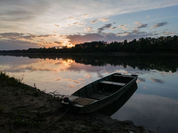 Boat moored in river against sky during sunset