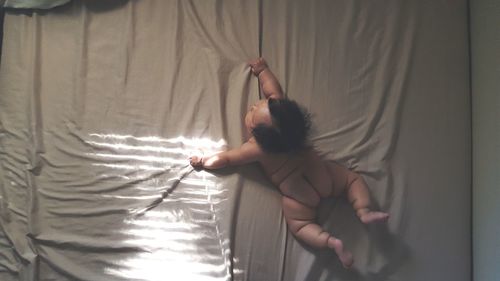 Rear view of naked baby girl lying on bed at home