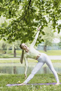 A young beautiful slender girl with long blonde hair does yoga in the summer in nature  in the park.