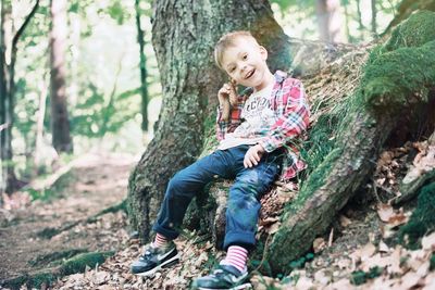 Full length of smiling girl sitting on tree trunk in forest