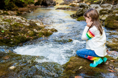 Full length of woman sitting on rock in stream