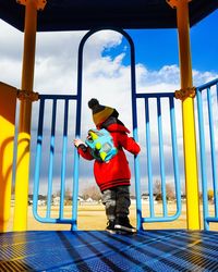 Side view of boy standing by umbrella against sky