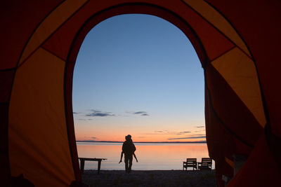 Silhouette people seen through tent at beach against sky