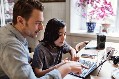 Father pointing at laptop while helping son in doing homework