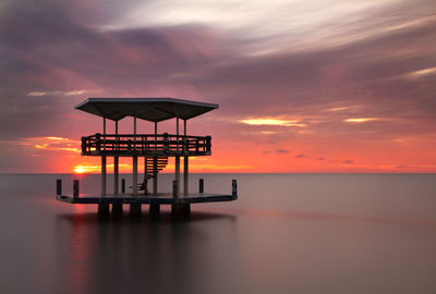 Lifeguard hut in sea against sky during sunset