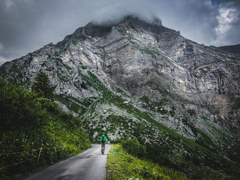 Rear view of man riding bicycle on road against mountains