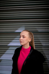 Beautiful young woman looking away while standing against wall