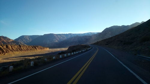 Empty road by mountains against clear blue sky