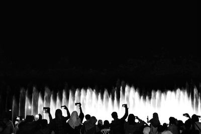 Rear view of people photographing fountain against clear sky at night