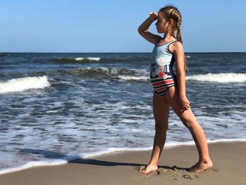 Full length of girl standing on shore at beach against sky during sunny day