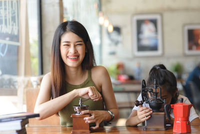 Portrait of smiling young woman with girl using coffee grinder