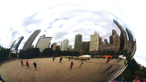 People by modern buildings in city against sky