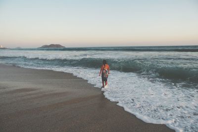 Rear view of woman standing at sea shore during sunset