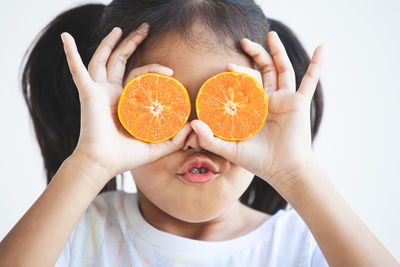 Close-up of girl holding orange slices against white background